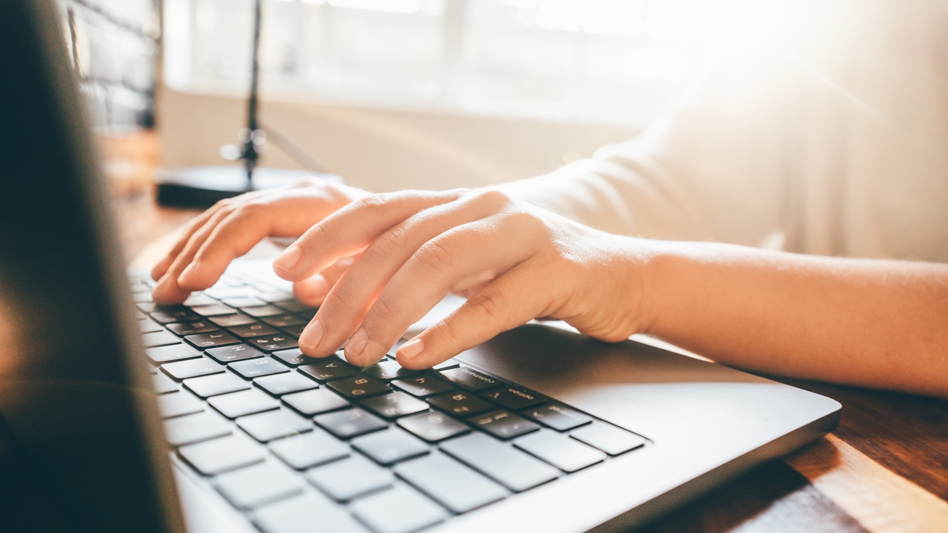 Close-up on hands using a laptop keyboard as woman works at a home office.